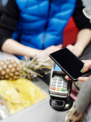 A customer uses a smartphone for contactless payment at a retail checkout with fresh produce.